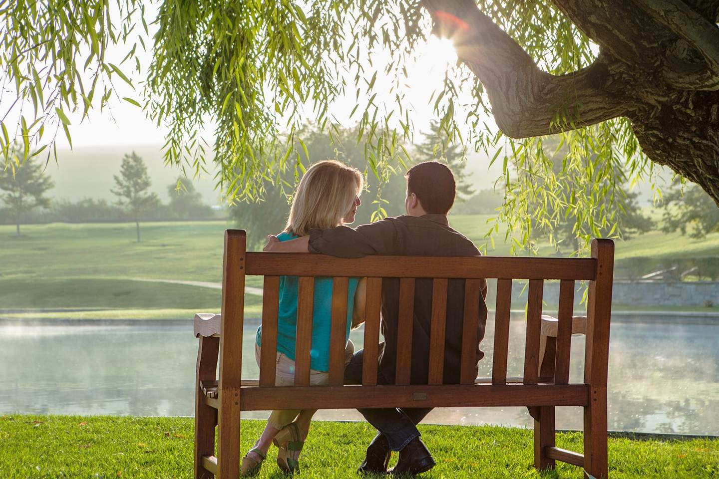 Couple sitting on bench under willow tree